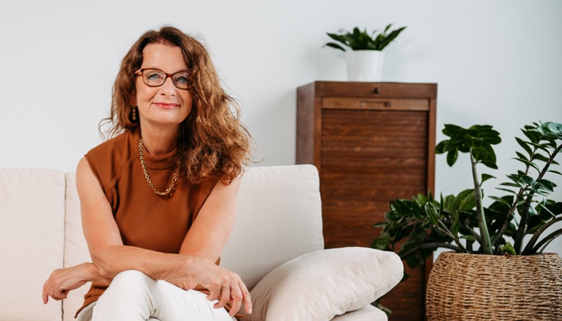 Eva Strübing sitzt auf dem Sofa und schaut direkt und offen in die Kamera