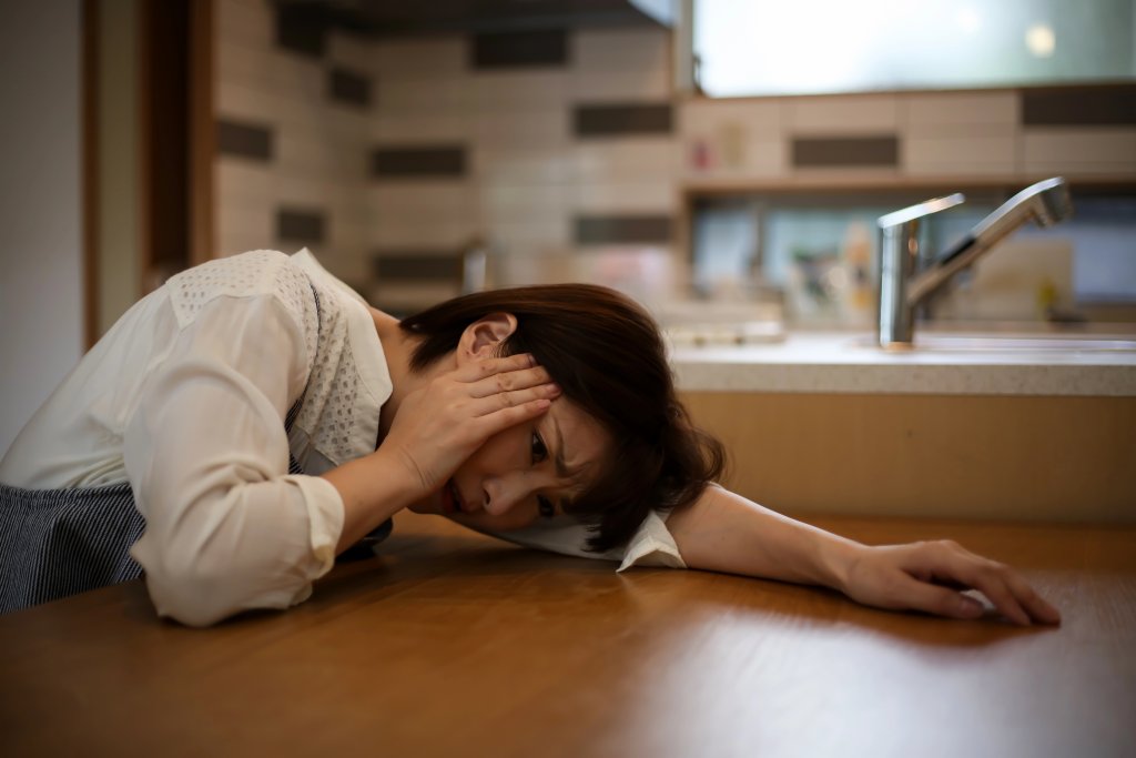 Frau legt Kopf auf dem Schreibtisch ab, hat Schmerzen